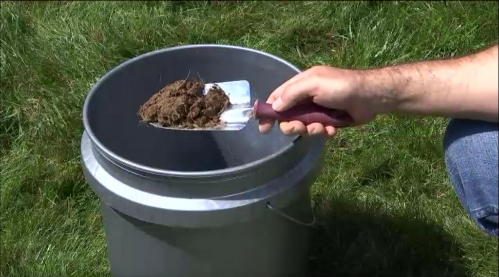 Gardening spade with dirt held over a bucket