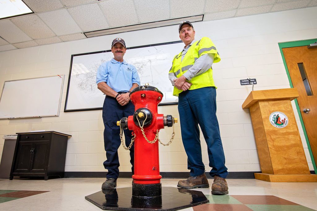 Two men standing behind a red & black fire hydrant